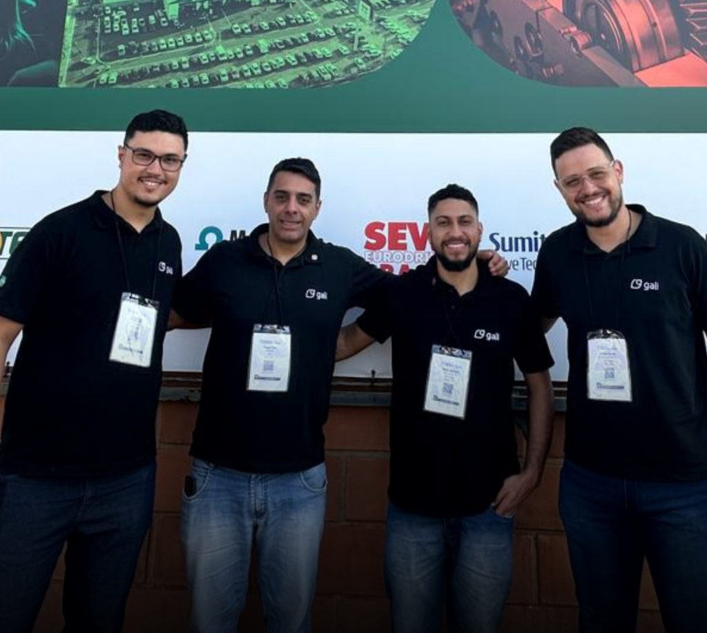 Quatro colaboradores da Gali posam sorridentes durante a Fenasucro & Agrocana 2025, evento de referência no setor de bioenergia. Todos vestem camisetas pretas com o logotipo da Gali e crachás de identificação.