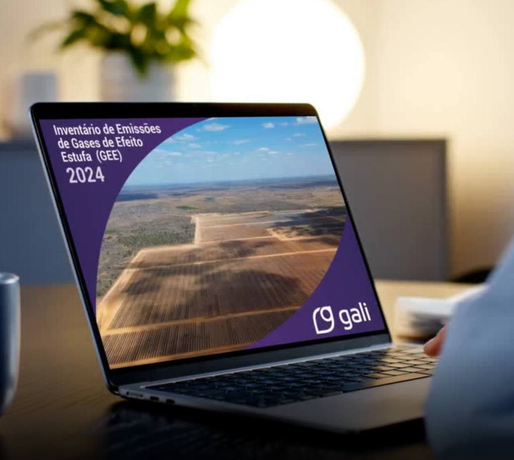 Notebook aberto exibindo na tela o relatório “Inventário de Emissões de Gases de Efeito Estufa (GEE) 2024”, da Gali. A apresentação mostra uma fotografia aérea de uma grande usina solar em meio a uma área extensa de solo claro. O design da tela tem fundo roxo, com destaque para o título do inventário no canto superior esquerdo e o logotipo da Gali no canto inferior direito.