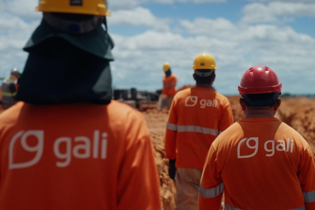 Colaboradores da Gali usando uniformes e capacetes em uma obra a céu aberto.