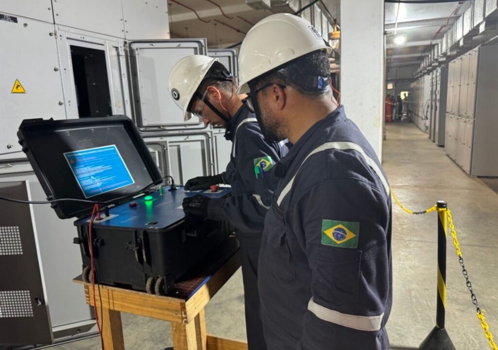Dois profissionais da Gali Energia com EPIs operando sistema de comissionamento em computador, realizando testes em gavetas e painéis CCM.